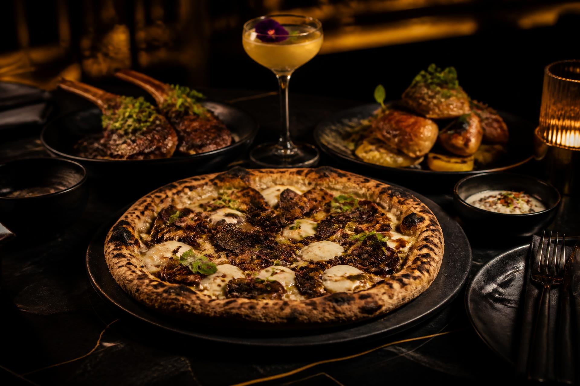 Vedugnsbakad pizza och grillrätter dukade på ett mörkt bord